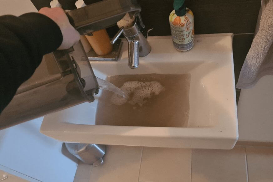 Wischroboter Schmutzwassertank stinkt: Nahaufnahme des trüben Tankinhalts nach einem Wischgang wird in ein Waschbecken ausgekippt